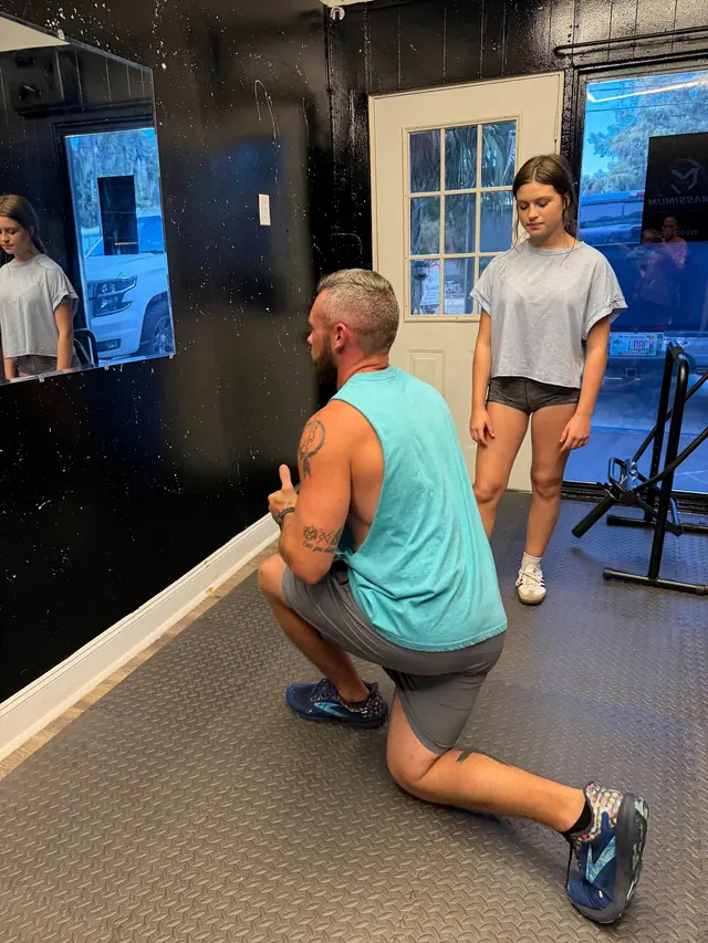 Coach Jared Massey kneeling to cue an athlete during a session at Massimum Sports Training in Tavares