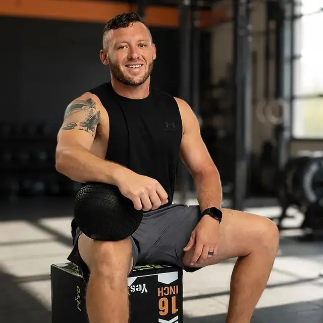 Coach Jared Massey, founder of Massimum Sports Training, seated on a plyo box holding a slam ball