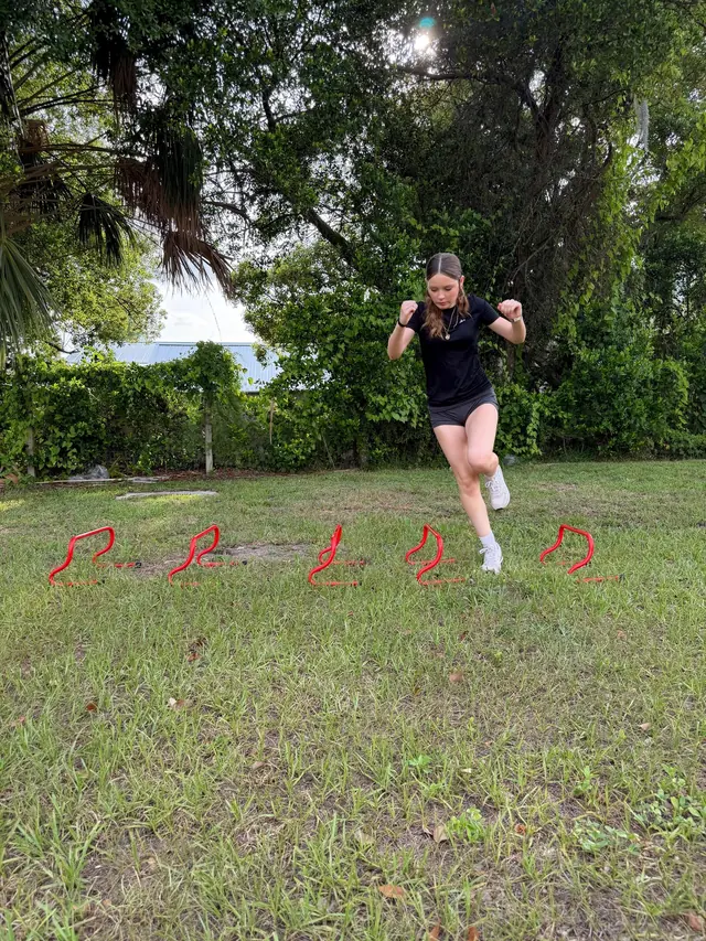 Athlete driving a knee through a mini hurdle drill on grass