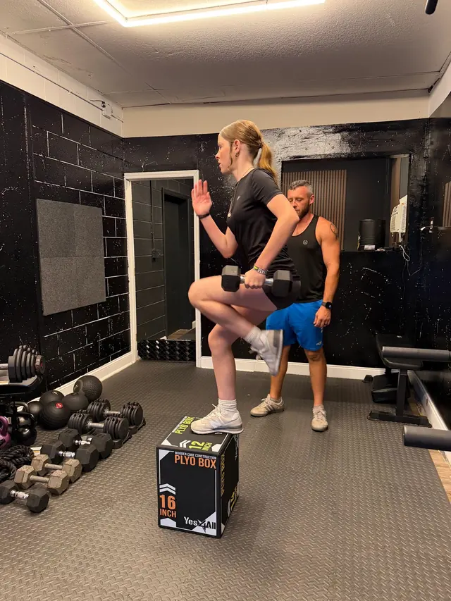 Athlete doing a weighted step-up on a plyo box while Coach Jared watches her form